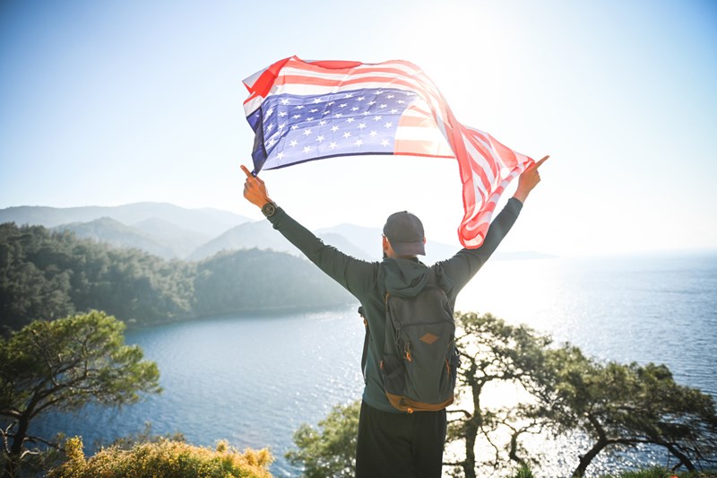Man_with_american_flag_on_the_background_of_the_sea_and_mountains